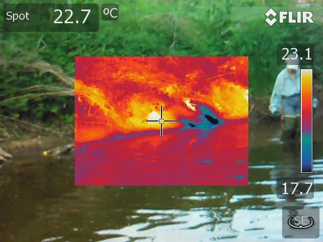 Thermal imagery blends into the surface of a river beside a person standing in the water.