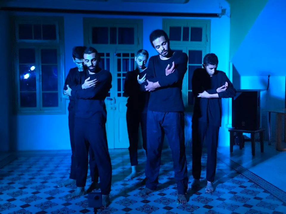 Three performers standing in blue light in a room.